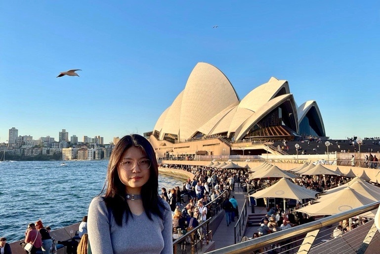 a young woman poses in front of Sydney Opera House