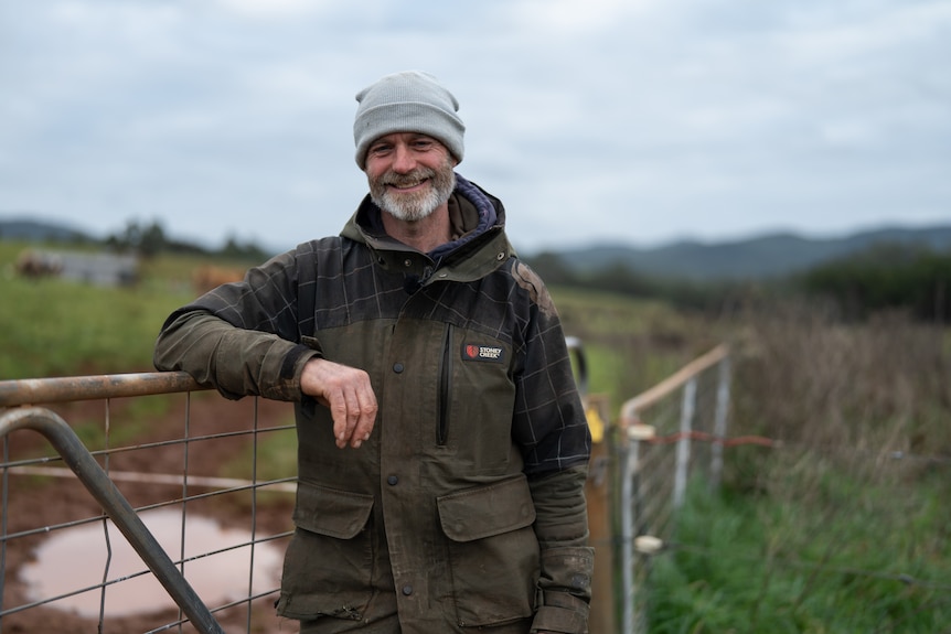 Man in beanie and coat leans against gate in paddock